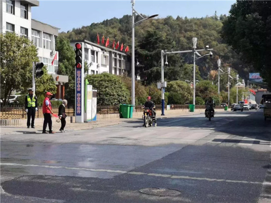 志愿者们头戴小红帽,身穿红马甲,手拿小红旗,站在交通路口进行文明交通引导
